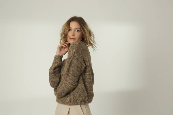 Fashion portrait of young woman in brown winter sweater and beige wide pants on the white background - Fotoğraf, Görsel