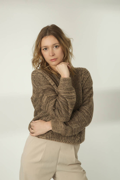 Retrato de moda de mujer joven en suéter de invierno marrón y pantalones anchos beige en el fondo blanco - Foto, Imagen