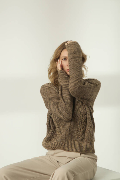 Fashion portrait of young woman in brown winter sweater and beige wide pants on the white background - 写真・画像