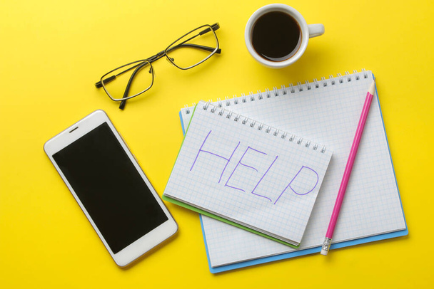 Notatnik z napisem pomoc, kawa i smartfon na jasnożółtym tle - Zdjęcie, obraz