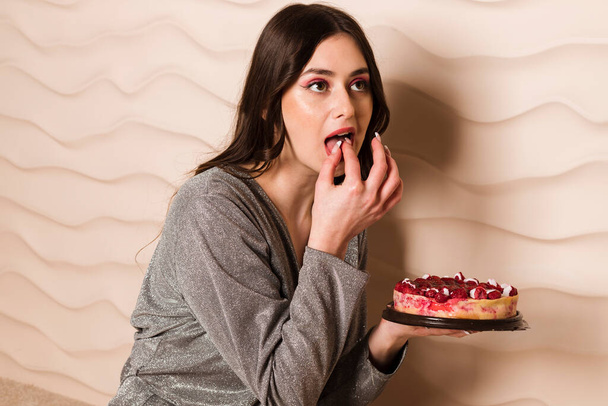 Gri bir arka plan üzerinde izole çikolatalı kek yiyip bitirecek aç genç hamile bir kadın portresi kapatın - Fotoğraf, Görsel