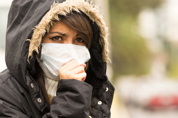 young girl walking wearing jacket and a mask in the city street concept of  pollution - Фото, изображение
