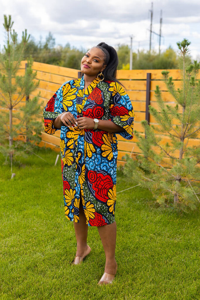 Arka bahçede dikilen kırmızı günlük giysili güzel Afrikalı Amerikalı kadının yaz portresi. Kenar mahalle yaşam tarzı ve hafta sonları kırsal konseptte rahatlama - Fotoğraf, Görsel