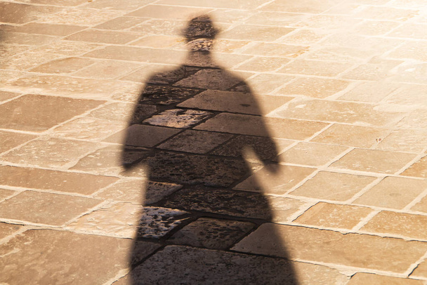 La mia ombra sul soleggiato territorio di Lecce, Italia. Lunga ombra di un uomo con un cappello, al tramonto su un pavimento di ciottoli beige. - Foto, immagini