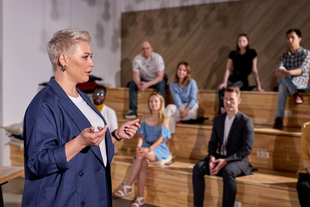 Confident Female speaker giving talk in conference hall at business meeting event. Group of people in audience at conference hall, listening to lesson. Business and entrepreneurship. copy space - Foto, Bild