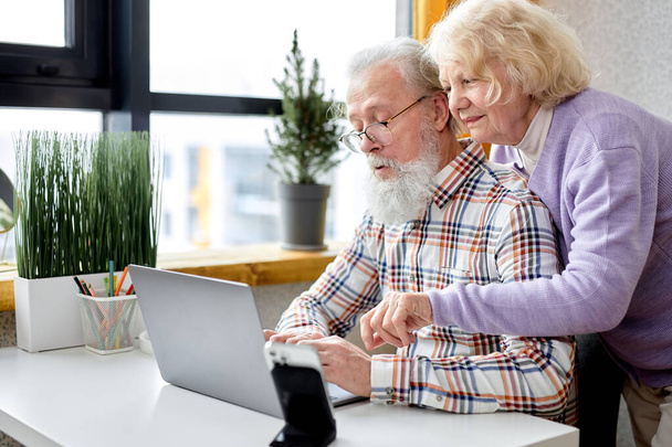 aged spouses using apps on laptop. Happy senior couple having fun online, surfing the Net. Senior people active social networks users spend time together, watching something interesting - Фото, изображение