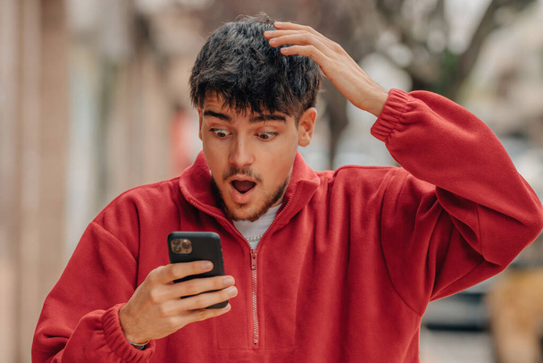 young man with mobile phone in the street with surprised expression - 写真・画像