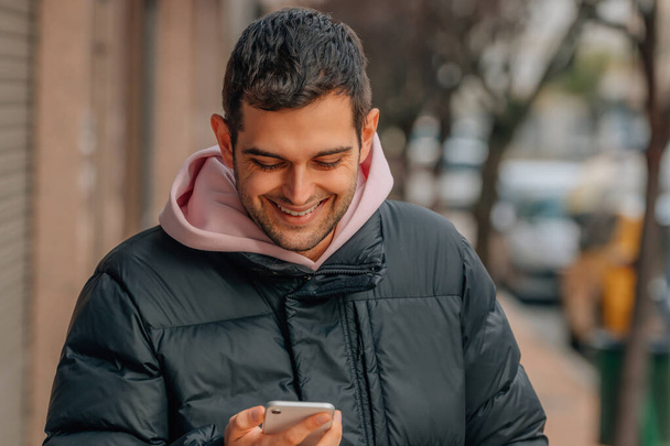 young man on the street with mobile phone excited celebrating success in warm clothes - Fotoğraf, Görsel