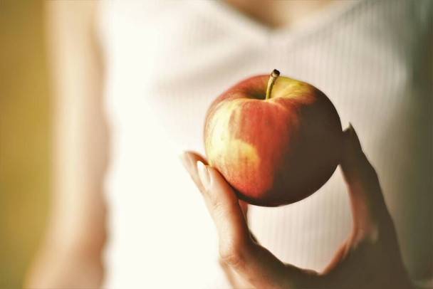 Červené jablko v ženských prstech na pozadí dívky v bílé košili - Fotografie, Obrázek