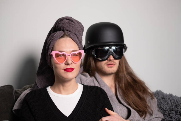 Young beautiful woman with red lips wearing pink sunglasses, young man with long hair wearing motorcycle glasses sunglasses, dark gray helmet on his head. - Photo, Image