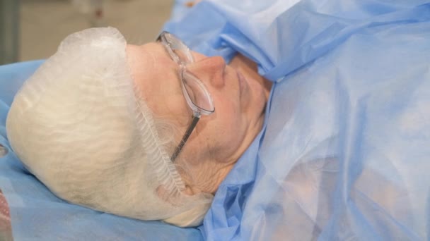 Portret van een zieke oudere vrouw op een bed in een ziekenhuis. Een patiënt die in een moderne kliniek wordt behandeld - Video