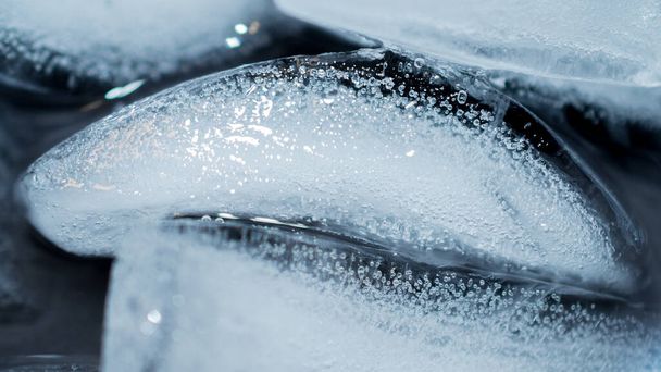 Kostka lodu unosząca się w drinku z bliska. Makro przejrzyste pęcherzyki lodu w szklance tła wody - Zdjęcie, obraz