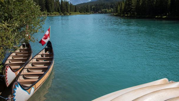 Bote en canoa atracado en la orilla. Agua turquesa del río Bow y fondo de la bandera de Canadá - Foto, imagen