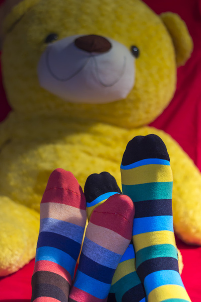 Цветные носки на ногах подростков над желтым плюшевым мишкой
 - Фото, изображение