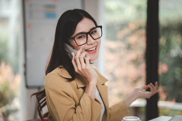 Asian woman talking on the phone, she is a salesperson in a startup company, she is calling customers to sell products and promotions. Concept of selling products through telephone channels. - 写真・画像