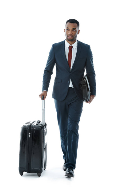 I hope Ive got everything...A handsome young african american businessman walking alongside his suitcase while isolated on white - Fotografie, Obrázek