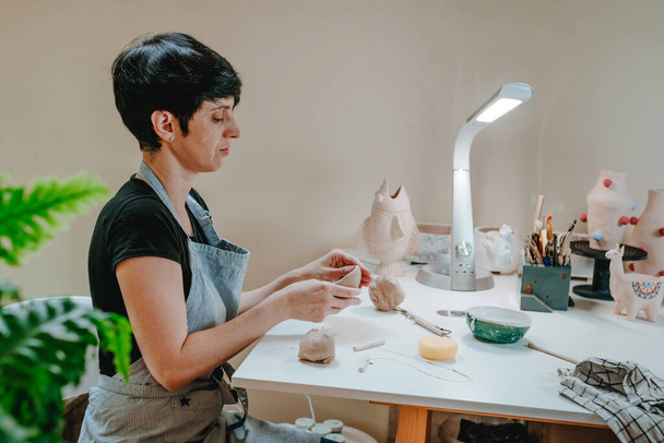 Jonge vrouwelijke pottenbakker beeldhouwt een beker met haar handen in haar werkplaats. Close-up van vrouwelijke handen. Selectieve focus. - Foto, afbeelding