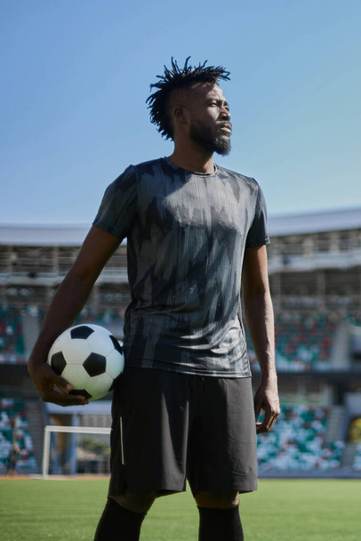 A young man stands in a stadium with a soccer ball in his hand - 写真・画像
