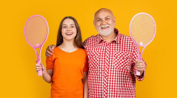 happy teen girl with grandfather with badminton racket on yellow background. - Фото, изображение