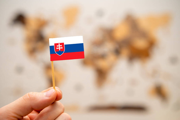 Slovakia flag in mans hand on the wooden world map background. Global economy and geopolitics concept.  - Photo, Image