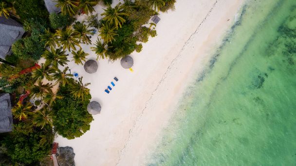 Μια πανέμορφη τροπική παραλία με λευκή άμμο, φοίνικες, τυρκουάζ ωκεανό ενάντια σε ένα μπλε ουρανό με σύννεφα σε μια ηλιόλουστη μέρα του καλοκαιριού. Το τέλειο σκηνικό για χαλαρωτικές διακοπές, Zanzibar Island. - Φωτογραφία, εικόνα