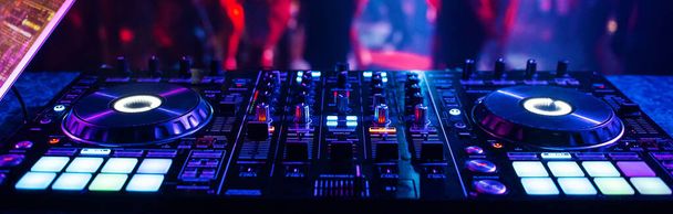 mezclador de DJ controlador de música en un club nocturno en una fiesta en el fondo de siluetas borrosas de personas bailando - Foto, imagen