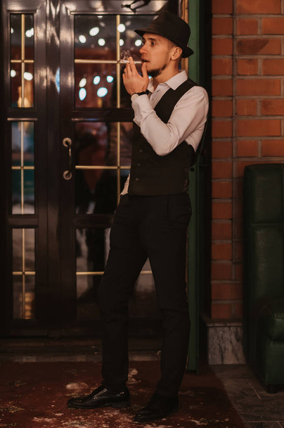 l'uomo elegante in un cappello fuma una sigaretta a porta all'ingresso di bar - Foto, immagini