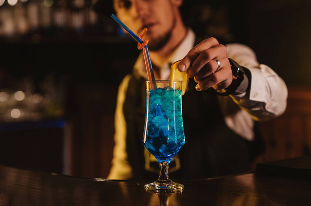 бармен подает коктейль Blue Lagoon в стакане с соломой у барной стойки в ресторане - Фото, изображение