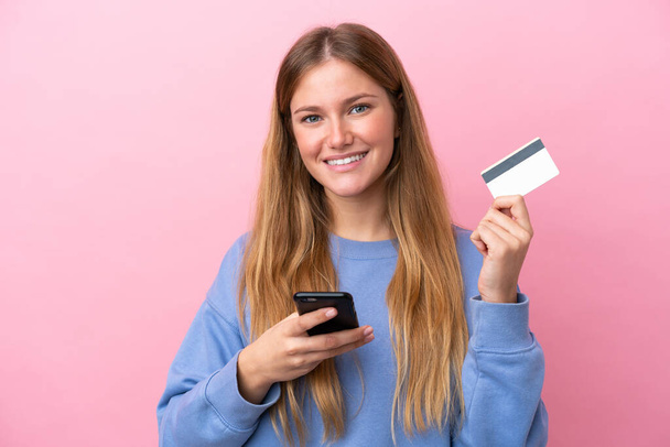 Young blonde woman isolated on pink background buying with the mobile with a credit card - Photo, Image