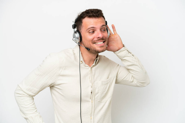 Telemarketer caucasian man working with a headset isolated on white background listening to something by putting hand on the ear - Φωτογραφία, εικόνα