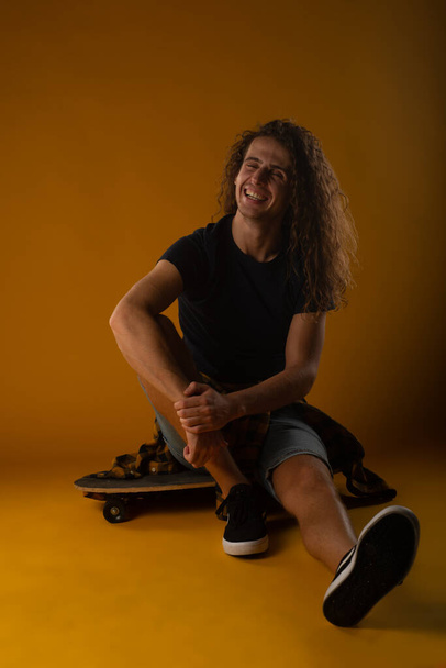 In forma e bel ragazzo seduto sul suo skateboard con uno sfondo giallo in studio - Foto, immagini