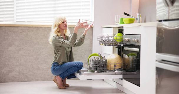Young Woman Taking Drinking Glass From Dishwasher In Kitchen - Foto, Imagen