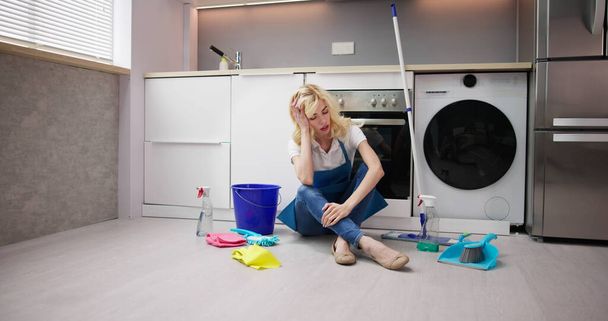 Frustrée jeune femme assise sur le plancher de la cuisine et regardant les produits de nettoyage à la maison
 - Photo, image