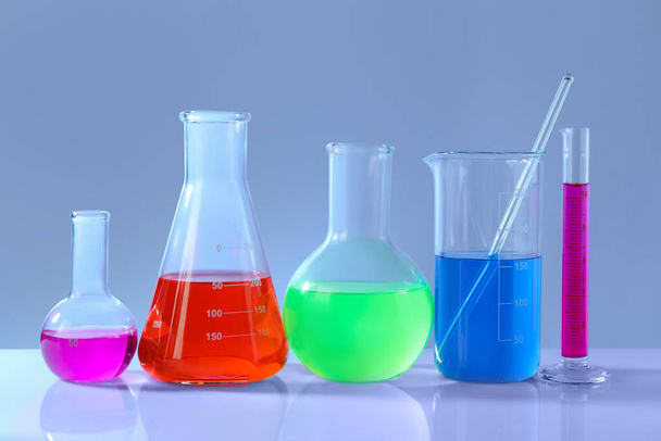 Different laboratory glassware with colorful liquids on white table against grey background - Fotografie, Obrázek