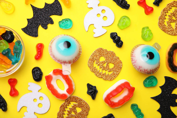 Tasty colorful jelly candies and Halloween decorations on yellow background, flat lay - Zdjęcie, obraz