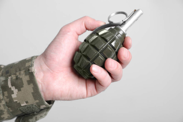 Soldier holding hand grenade on light grey background, closeup. Military service - Фото, изображение