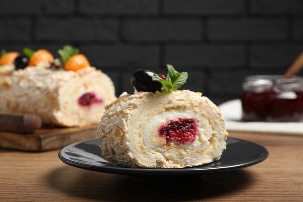 Slice of tasty meringue roll with jam, tangerine slices and mint leaves on wooden table - Photo, image