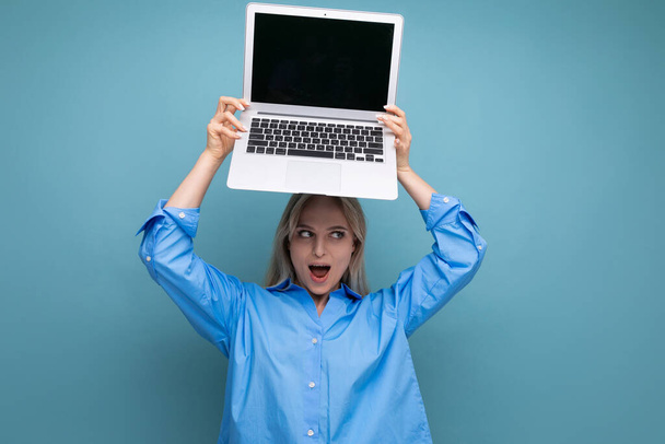 foto de sorprendida chica rubia linda sorprendida con portátil abierto con espacio en blanco para el sitio web en fondo azul. - Foto, Imagen