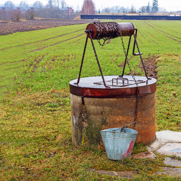 Egy régi kút, fém borítással és görgővel, egy vödör, ami vizet gyűjt a vidéken tavasszal. - Fotó, kép