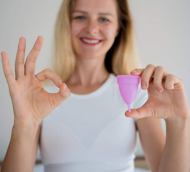 Young beautiful woman at home holding a menstrual cup in her hands. - Foto, imagen