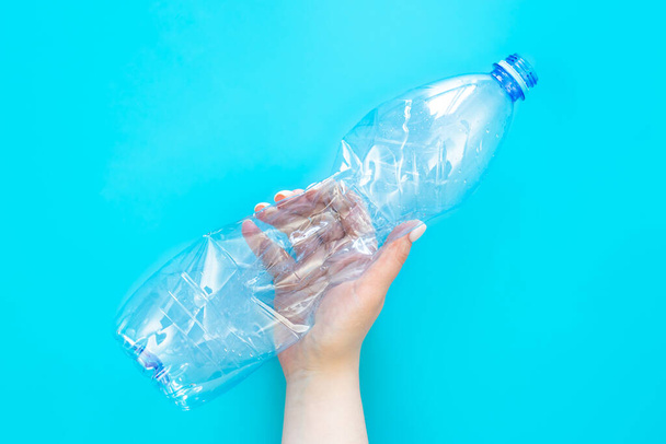 Used plastic bottle in a female hand on a blue background, top view, flat lay. The concept of using plastic. Environmental problem, global environmental problem, copy space. - 写真・画像