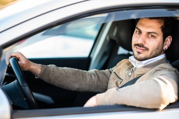 Handsome young man in his car. Smiling while driving a car - 写真・画像