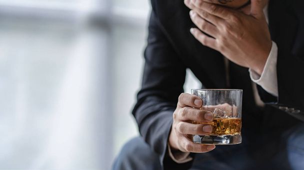Closeup of stressed businessman holding glass of whiskey sitting sad alone at desk Alcohol addiction and drunken businessman concept - Photo, Image