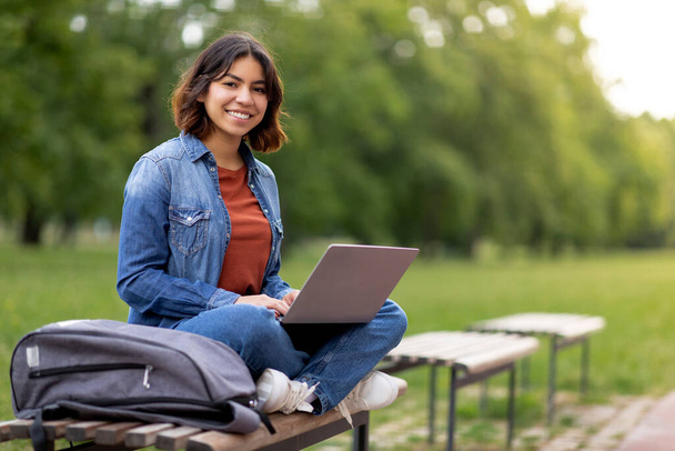 Gyönyörű mosolygó arab Nő Diák Laptop használata közben pihentető padon szabadban, vidám fiatal közel-keleti nő tanulmány Online a számítógépen, Felkészülés a vizsgára kívül Városligetben, Másolás tér - Fotó, kép