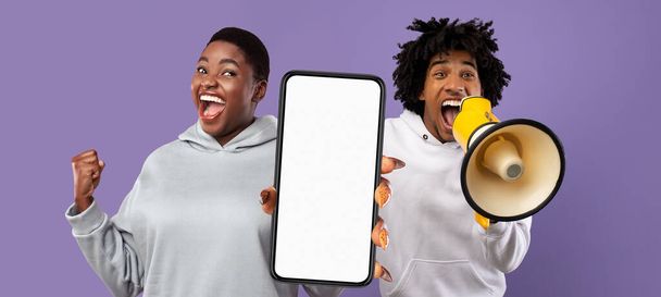 Захоплений чорний чоловік і жінка, що використовує мегафон і показує великий порожній смартфон, афро-американську чоловічу та жіночу рекламу онлайн-пропозицію або веб-сайт, стоячи на фіолетовому фоні, макет
 - Фото, зображення