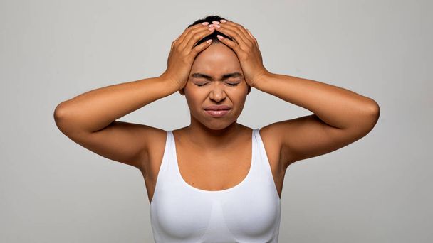Unhappy sick young african american woman suffer from terrible strong head pain, touching her head with closed eyes, studio shot, black lady have migraine, grey background, copy space - Photo, image