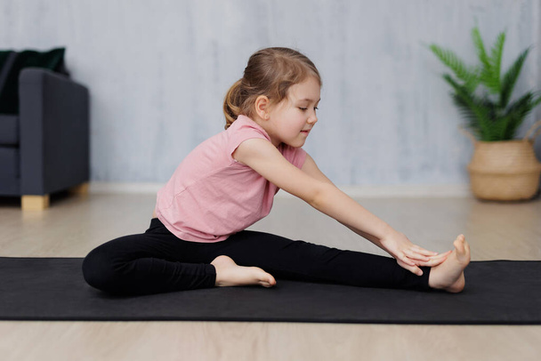 portrait of cute little girl doing stretching exercises on yoga mat at home - Foto, Imagem