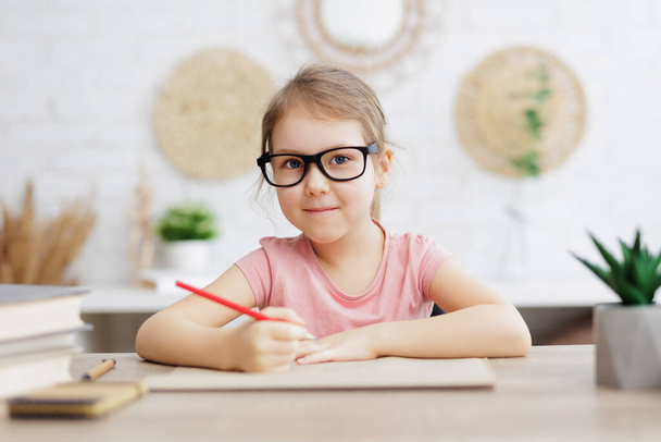 Kindheits- und Bildungskonzept - süßes kleines Schulmädchen macht Hausaufgaben zu Hause - Foto, Bild