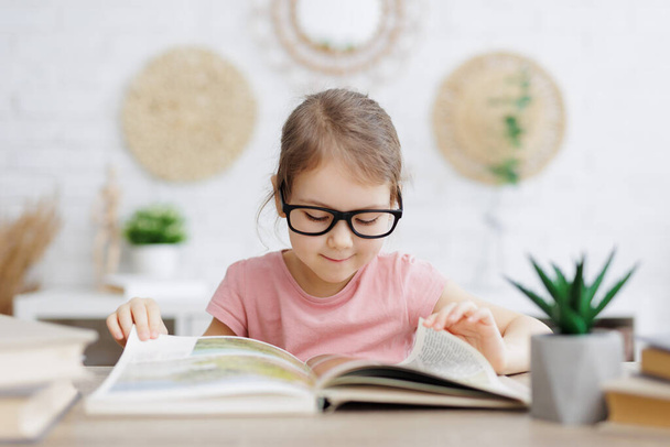 παιδική ηλικία και την εκπαίδευση έννοια - χαριτωμένο μικρό μαθητριούλα ανάγνωση βιβλίο στο σπίτι - Φωτογραφία, εικόνα