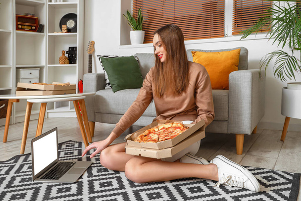 Young woman with tasty pizza and laptop sitting on floor at home - Foto, Imagen